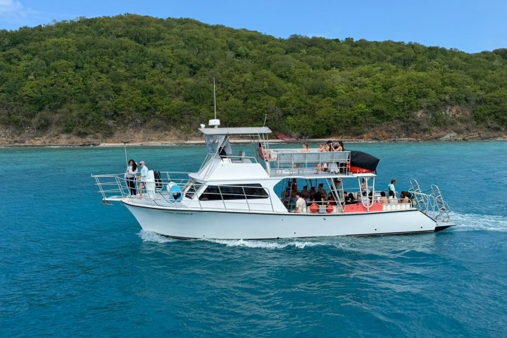 A white boat with passengers sails on turquoise water near a green, forested island.