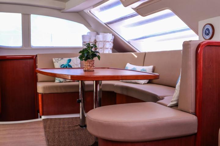 Cozy boat interior with a corner dining area, brown seating, wooden table, and potted plant.