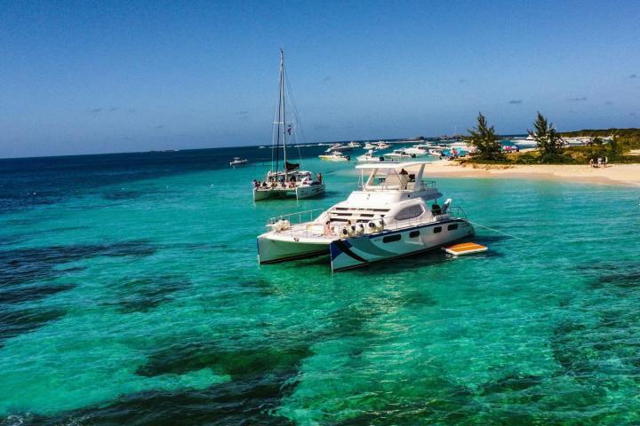 Boats anchored on clear turquoise water near a sandy beach.