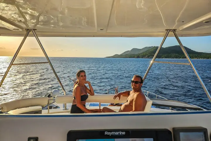 Two people relaxing on a boat at sea with mountains in the background.