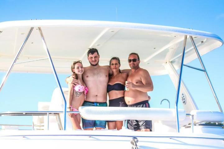 Four people smiling on a boat with a canopy, under a clear blue sky.