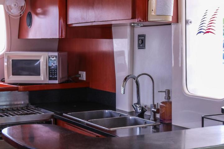 Yacht kitchen with wooden cabinets, stove, microwave, sink, and window.